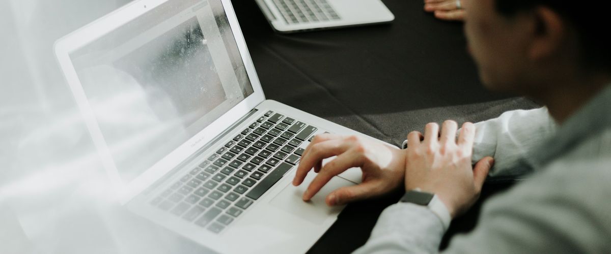 A person typing on a silver laptop at a dark table